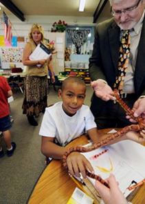 Principal Ben Januschka and student Jayvon Maternowski share hold of a corn snake in the first grade classroom of Dawn Slinger, background left.